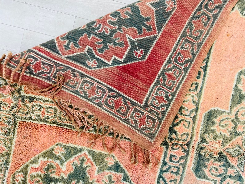May include: A close-up of a pink and green patterned rug with a fringe. The rug has a geometric design with a central medallion.