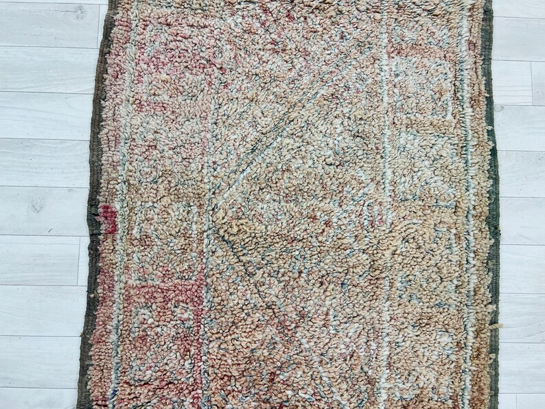 May include: A vintage rug with a faded, geometric pattern in shades of beige, brown, and pink. The rug has a distressed, worn look, adding to its unique character.