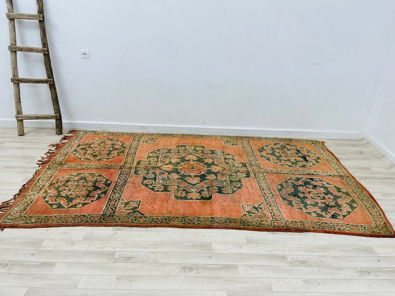 May include: A vintage rug with a geometric pattern in shades of orange, green, and brown. The rug has a fringed edge and is made of wool.