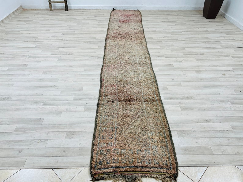 May include: A long, narrow rug with a faded, multi-colored pattern. The rug has a fringe on both ends and is made of a woven material.