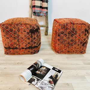 K&ouml;nnte beinhalten: Zwei quadratische orangefarbene und schwarze Poufs mit einem wei&szlig;en Rand. Die Poufs stehen auf einem hellen Holzboden.