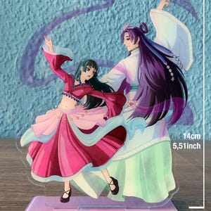 May include: A clear acrylic stand with two anime characters. The female character is wearing a pink and red dress with a blue sash. The male character is wearing a white and green robe with long purple hair. The stand is 5.51 inches tall and 4.33 inches wide.