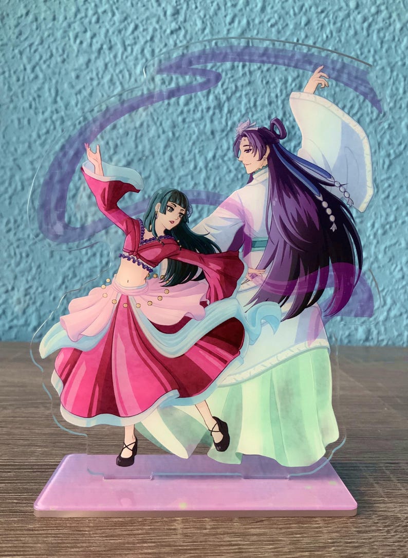 May include: A clear acrylic stand with a purple base features a hand-painted illustration of two anime characters dancing. The female character wears a pink and red dress with a blue sash. The male character wears a white and green robe with long purple hair.