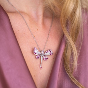 May include: A silver chain necklace with a pink and white dragonfly pendant. The dragonfly is made of sparkling gemstones.