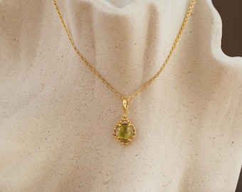 May include: A gold necklace featuring a delicate chain and a pendant with a central oval-shaped light green gemstone. The stone is encased in a decorative gold frame with small beaded details along the edges, creating a refined and classic appearance.