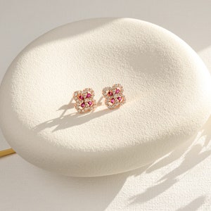 May include: A pair of rose gold earrings with a square design featuring a cluster of small clear and pink gemstones.