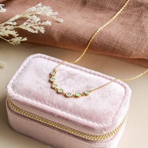 May include: A gold necklace with a curved row of seven opal stones. The necklace is displayed in a pink velvet jewellery box.