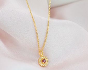 May include: A gold chain necklace with a pendant featuring a small red gemstone surrounded by a circle of smaller white gemstones.