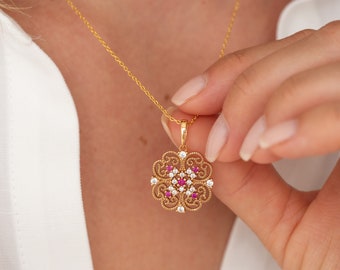 May include: A gold necklace with a delicate pendant featuring a filigree design with white and pink gemstones.