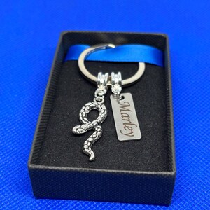May include: A silver snake keyring with a silver tag engraved with the name "Marley". The keyring is in a black gift box with a blue ribbon.