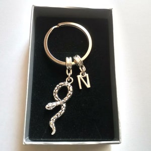 May include: Silver key ring with a snake charm and a letter N charm. The keyring is displayed in a black velvet box.