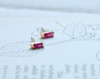 May include: A pair of gold stud earrings with a rectangular pink gemstone.