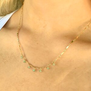 May include: A gold chain necklace with small green gemstone charms hanging from it.