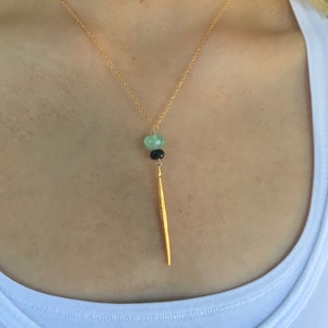 May include: A gold chain necklace with a green and black gemstone pendant and a long, thin gold bar hanging from it.