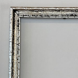 May include: A rectangular silver picture frame with ornate detailing. The frame has a textured, speckled appearance with a decorative border. The frame is empty, with a light gray background visible through the opening.