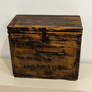 May include: A dark brown wooden storage box with a hinged lid and a metal latch. The box has a distressed look with visible wood grain and black paint.