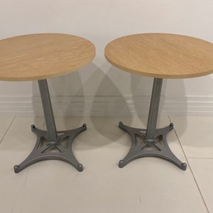 May include: Two round wooden tables with grey metal bases. The tables have a simple design and are perfect for a small space.