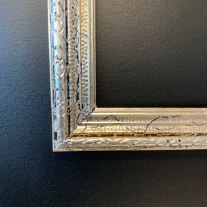 May include: A silver picture frame with a decorative, ornate border. The frame has a distressed, aged look with a crackled finish.