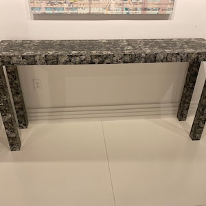 Op de afbeelding: Een lange, smalle consoletafel met een zwart-wit gepatroneerd blad en poten. De tafel is gemaakt van hout en heeft een modern ontwerp.