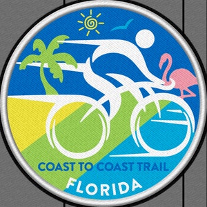May include: A white bicycle with a person riding it, a palm tree, a sun, and a pink flamingo. The background is blue, green, and yellow. The text "COAST TO COAST TRAIL FLORIDA" is at the bottom of the image.