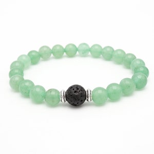 May include: A beaded bracelet featuring light green, round gemstone beads. The bracelet has a central black lava stone bead, accented with silver-colored metal spacers. The beads are strung on an elastic band, creating a stretchable design.