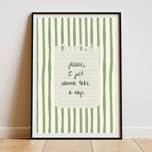 Op de afbeelding: Ingelijste kunstdruk met een zwarte rand. De achtergrond heeft verticale groene strepen. Een gescheurde papieren notitie is gecentreerd en toont de handgeschreven tekst: "please, I just wanna take a nap."
