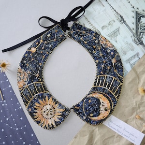 Puede incluir: Un collar de cuentas azul y dorado con un diseño de sol y luna. El collar está hecho de cuentas pequeñas y presenta un tema celestial.