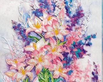 May include: A beaded floral artwork depicting a bouquet of lilies and other flowers in shades of pink, white, purple, and blue. The flowers have yellow centres and green leaves, set against a soft, watercolour-like background.
