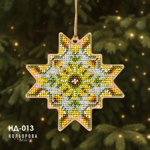 May include: A star-shaped wooden ornament featuring a beaded mosaic pattern in shades of yellow, green, white, and brown. The design includes a central floral motif with radiating points. A light-colored string is attached for hanging. Text reads НД-013 КОЛЬОРОВА.