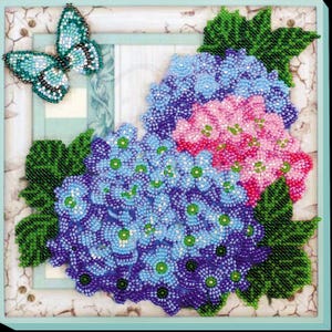 Puede incluir: Primer plano de un diseño de bordado con cuentas que presenta una mariposa azul y un ramo de hortensias rosas y azules.