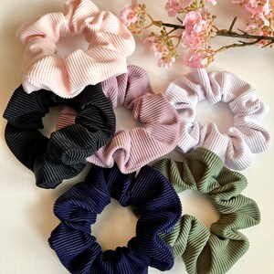 May include: Six colorful scrunchies made of ribbed fabric. The scrunchies are in shades of pink, purple, white, black, blue, and green.