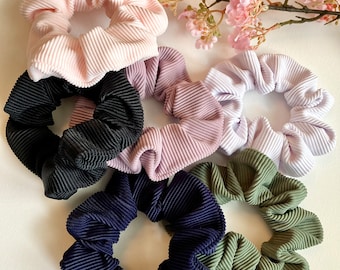 May include: Six colorful scrunchies made of ribbed fabric. The scrunchies are in shades of pink, purple, white, black, blue, and green.