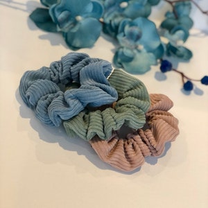 Puede incluir: Tres scrunchies en colores azul, verde y marr&oacute;n. Los scrunchies est&aacute;n hechos de una tela suave y texturizada.