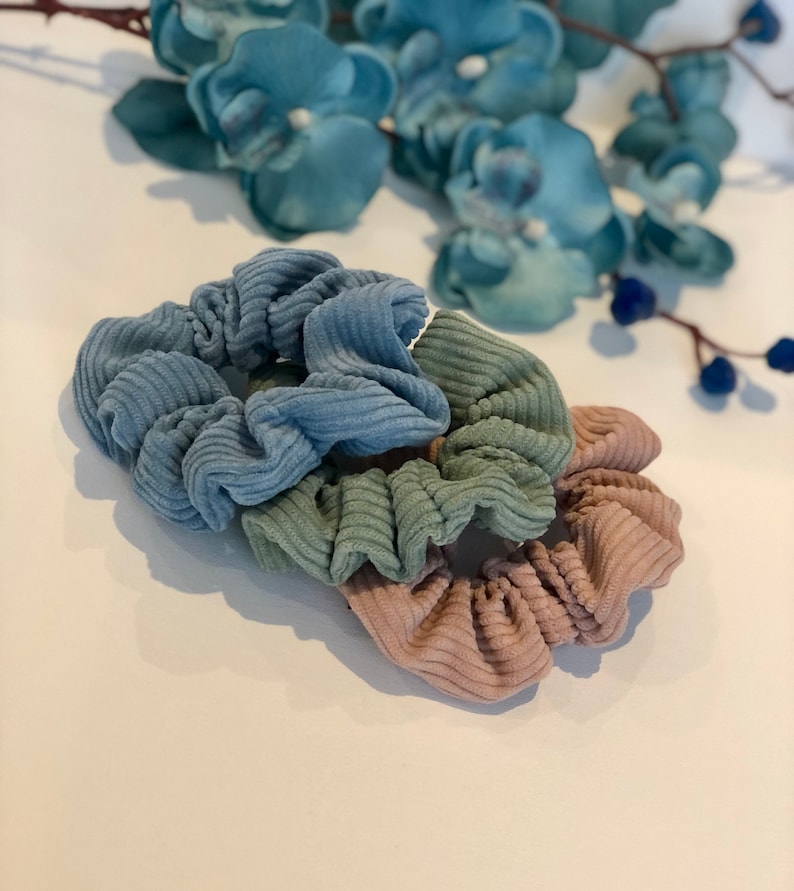 Puede incluir: Tres scrunchies en colores azul, verde y marr&oacute;n. Los scrunchies est&aacute;n hechos de una tela suave y texturizada.