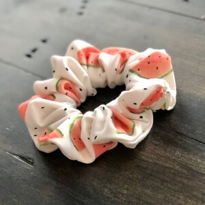 May include: White scrunchie with a watermelon print. The scrunchie is made of soft fabric and has a gathered look.