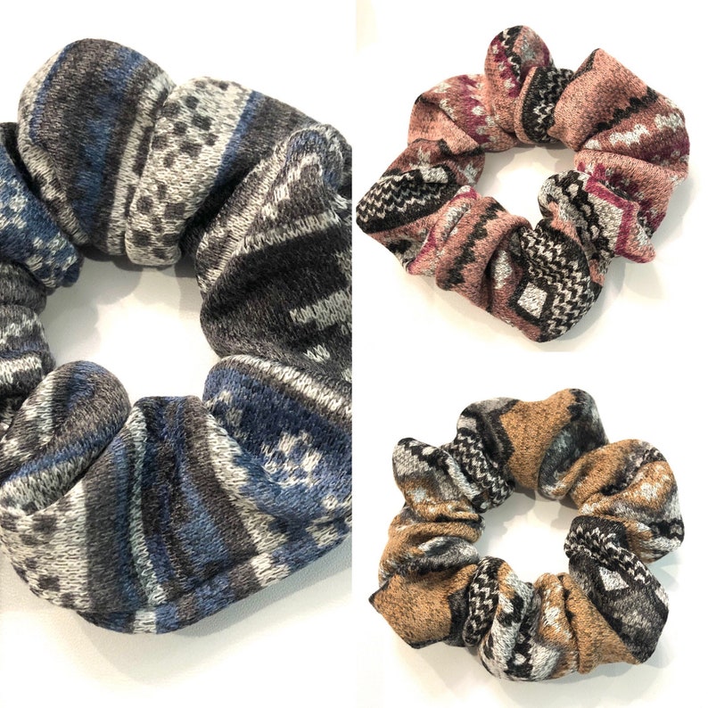 May include: Three patterned scrunchies in different colors. The scrunchies are made of a soft, fuzzy fabric and have a geometric pattern. The colors are gray, pink, and brown.