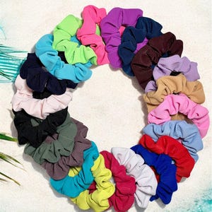May include: A collection of 24 colourful scrunchies in a variety of colours, including pink, blue, green, red, and purple. The scrunchies are arranged in a circle on a white surface.