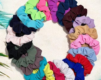 May include: A collection of 24 colorful scrunchies in a variety of colors, including pink, blue, green, red, and purple. The scrunchies are arranged in a circle on a white surface.