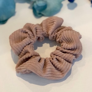 Puede incluir: Una scrunchie para el pelo de color marr&oacute;n claro de pana.