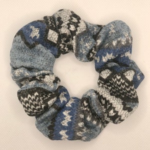 May include: A blue, black, and white patterned scrunchie made of soft, knitted fabric.