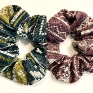 May include: Two patterned scrunchies, one in green, white, and gold, and the other in purple, white, and gray.