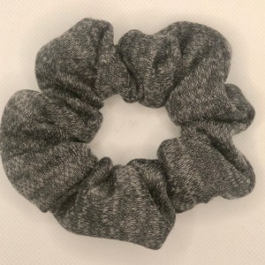May include: A gray and white scrunchie made of soft, textured fabric. The scrunchie is in the shape of a circle and has a ruffled appearance.