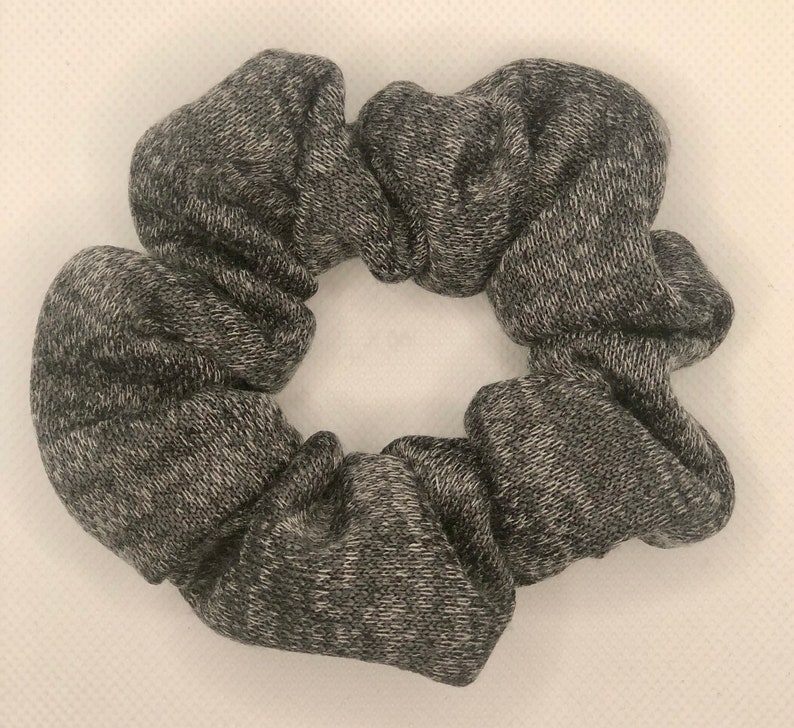 May include: A gray and white scrunchie made of soft, textured fabric. The scrunchie is in the shape of a circle and has a ruffled appearance.