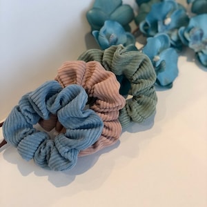 Puede incluir: Tres scrunchies en diferentes colores: azul claro, rosa y verde. Los scrunchies est&aacute;n hechos de una tela suave y texturizada.