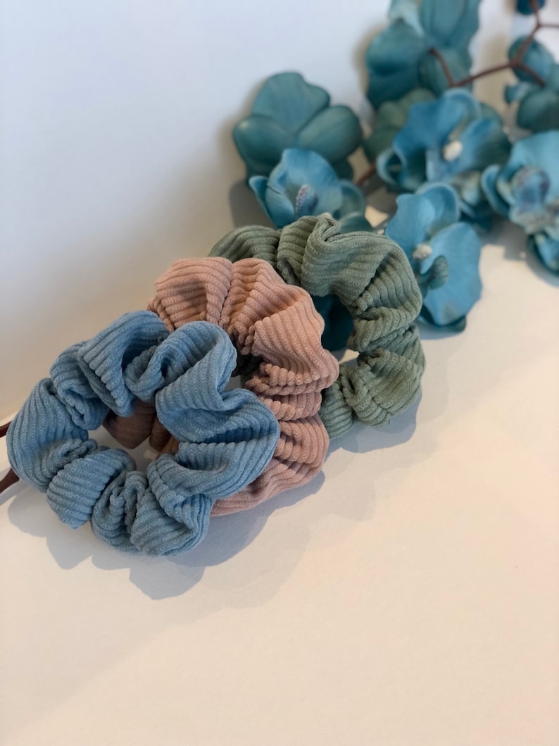 Puede incluir: Tres scrunchies en diferentes colores: azul claro, rosa y verde. Los scrunchies est&aacute;n hechos de una tela suave y texturizada.