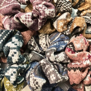 May include: A collection of colorful knitted hair scrunchies with various patterns. The scrunchies are made of soft, fuzzy material and are perfect for adding a touch of style to any hairstyle.