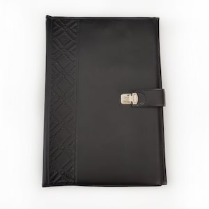 Puede incluir: Carpeta de cuero negro con un patrón de diamantes en relieve en el lado izquierdo. Cuenta con un cierre de broche plateado y una correa de cuero negro. La cubierta es rectangular y parece nueva.