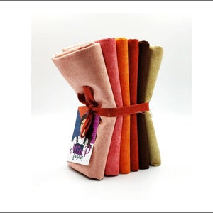 Puede incluir: Un conjunto de seis cuadrados de tela en varios tonos de naranja, rojo y marrón. La tela está atada con una cinta roja y una etiqueta que dice "Miss P Fabrics".