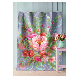 Puede incluir: Una colcha de diseño floral pixelado de colores con fondo gris. La colcha está colgada en una pared azul claro con una pequeña mesa rosa y un jarrón de flores delante.