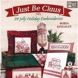 Könnte beinhalten: Ein Buch mit dem Titel "Just Be Claus" mit 24 fröhlichen Weihnachts-Stickereien von Robin Kingsley. Der Umschlag zeigt einen rot-weiß karierten Hintergrund mit verschiedenen gestickten Motiven, darunter den Weihnachtsmann, ein Weihnachtsdorf und ein Herz mit dem Text "Christmas Comes from the Heart".